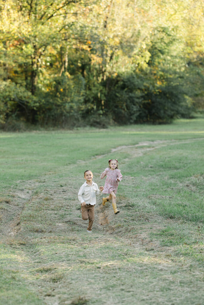 two kids running quickly toward the camera from across an open field during their family fall photo session in east texas