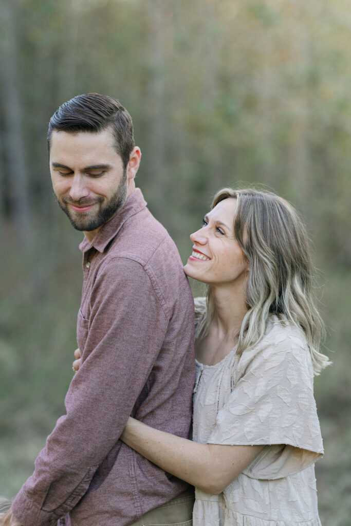 Mom and dad hugging in the golden sunset light in the tall trees during a family session in east texas