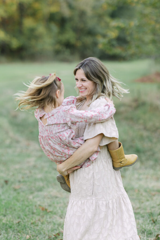 Mom twirling her daughter during fall family photos in an open field