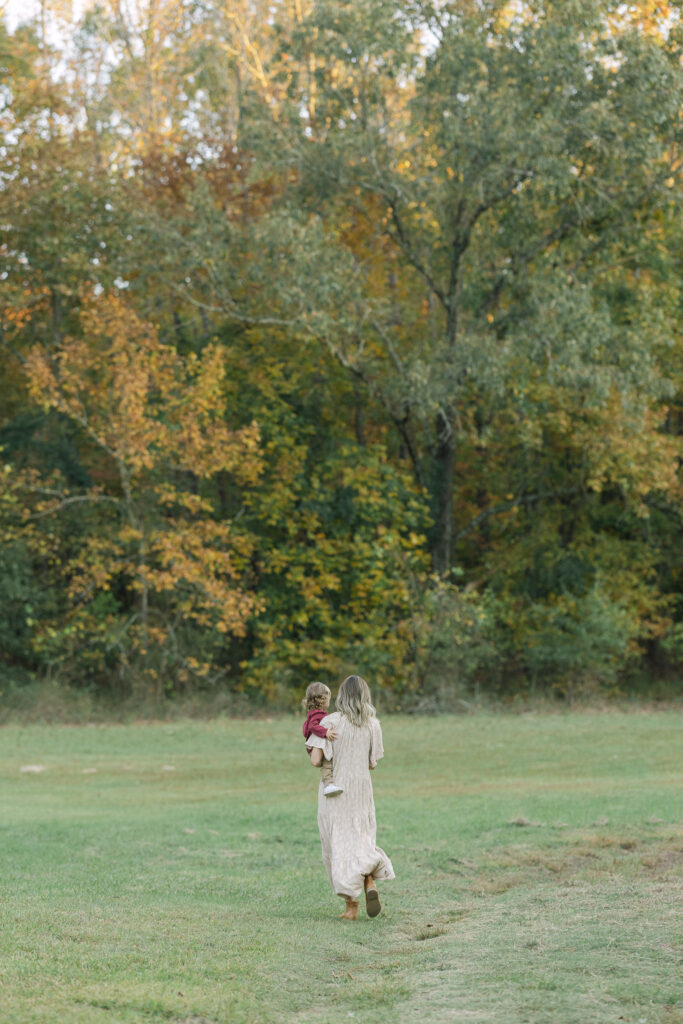 mom walking away from the camera with her youngest son on her hip during a family fall session in east texas
